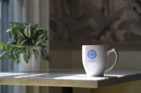 Coffe mug with Ellery Hotel logo on table near the window