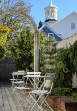 Outdoor enterance with white chairs and table surrounded by greenery