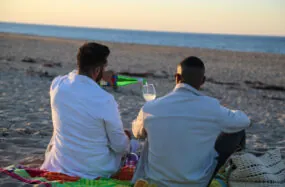 Two men sitting on beach at sunset